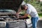 A bearded man leaned over the open hood of a black car with a screwdriver during the repair process. Diagnosis and replacement