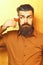 Bearded man, long beard. Brutal caucasian surprised hipster with moustache in brown shirt holding alcoholic red shot on