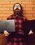 Bearded man, long beard. Brutal caucasian surprised unshaven hipster holding laptops in red black checkered shirt with