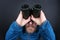 The a bearded man looks up through binoculars on grey background