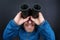 Bearded man looks up through binoculars on grey background