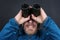 Bearded man looks up through binoculars on grey background