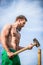 Bearded man with a naked torso with a sledge hammer works the garden a background of blue sky