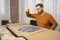 Bearded man in an orange sweater dropping little puzzle pieces while trying to put it together having fun