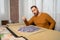 Bearded man in an orange sweater dropping little puzzle pieces while trying to put it together having fun