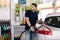 Bearded man refuelling car on gas station and looking into his smartphone. Man compares fuel prices