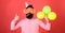 Bearded man showing thumb up gesture. Man with trendy beard blowing party whistle. Hipster with colorful balloons on red