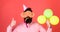 Bearded man showing thumb up. Man with trendy beard blowing party whistle. Hipster with colorful balloons on red