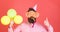 Bearded man showing thumb up. Man with trendy beard blowing party whistle. Hipster with colorful balloons on red