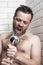 Bearded man singing in the bathroom using the shower head with f