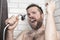 Bearded man singing in the bathroom using the shower head with f