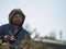 Bearded man sits against the sky and the forest in the hood and holds a camera in his hands