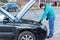 A bearded man standing next to the open hood of a black car during the repair process. Machine self service