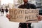 Bearded man is standing on street and holding a cardboard. It says homeless please help. Guy is looking for some mercy