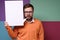 Bearded man with a strange expression on his face is holding a blank, white board, advertising space or announcement.