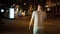 Bearded man in striped white and black t shirt and green shorts walking on the street at night and talk by mobile phone