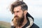 Bearded man on windy mountain top on natural cloudy sky