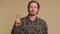 Bearded optimistic young man showing victory sign, hoping for success and win, doing peace gesture