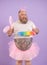 Bearded plump man in fairy costume holds colorful pp duster on purple background