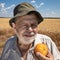 Bearded senior farmer ready to eat organic yellow tomato standing in wheat field