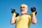 Bearded Senior sportman exercising with lifting dumbbell on blue sky background. Isolated, copy space. Senior man