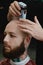 Bearded skinhead man in barbershop. Barber shaves head with electric trimmer.