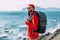 A bearded traveler with a backpack on the background of the sea. Portrait of a traveler in red clothes and sunglasses. A tourist