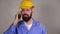 Bearded worker in helmet talking on the phone with someone on grey background