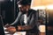 Bearded young businessman working in loft space at night. Coworker sits by the wooden table with lamp and office tools