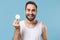 Bearded young man 20s years old in white shirt hold in hand cotton pad isolated on blue pastel wall background, studio