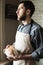 Bearded young man in rustic apron holding a loaf of bread in his hands