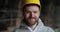 bearded young man in white coat and yellow helmet look in to the camera and smiles. factory engineer. master in the