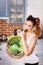 Beatiful caucasian girl in sporty wear holding basket of fresh vegetables and bites cucumber.