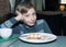 Beatiful funny child sitting in a restaurant eating cake and smiling