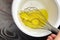 Beating raw yellow egg yolks with a handle steel whisk in white bowl on wooden table. Mixing food ingredients. Cooking chicken