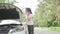 Beauitful woman looking under the hood of her broken car on countryside road