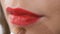 Beautician corrects the make-up around woman`s lips with red lipstick