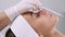 A beautician examines a female patient at the aesthetic medicine clinic. The beautician uses a pencil to measure facial