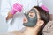 Beautician makes a black clay mask to rejuvenate the skin to beautiful woman.Cosmetology concept and treatment of problem skin