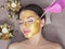 Beautician makes a golden mask to rejuvenate the skin to beautiful woman. Next to her are Christmas decorations.New Year`s and