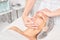 Beautician massages cream mask into woman face skin for rejuvenation, procedure in beauty salon