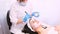 Beautician in a medical mask and gloves with a silicon brush applies a white moisturizing facial mask to the face of a