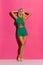 Beautifil Blond Woman In Green Short Jumpsuit And High Heels Is Standing With Hands Behind Head