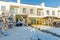 Beautifil exterior view of townhouseswith front yard covered with snow. White and yellow on blue sky background.