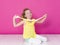 Beautiful 10 year old girl is playing with yellow slime in front of pink background and is happy