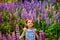 A beautiful 5-year-old girl in a field with lupines throws flowers in the air. A meadow with purple flowers and a little girl with