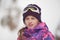 Beautiful active smiling happy small young caucasian girl in woolen hat and snowboarding jacket with ski googles during winter