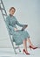 Beautiful adult business woman posing on a grey background while sitting on a ladder and holding a laptop