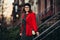 Beautiful adult woman leaves house and walking to the work smiling and enjoying the new day wearing classic red jacket, hat