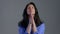 Beautiful adult woman praying over grey background. Lady in blue shirt begging someone with hope in eyes